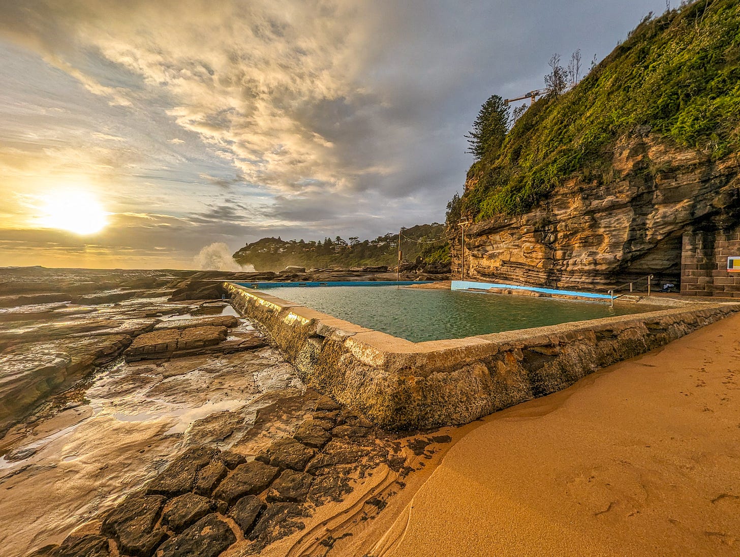 Whale Beach rock pool at sunrise. Water is calm and green. 