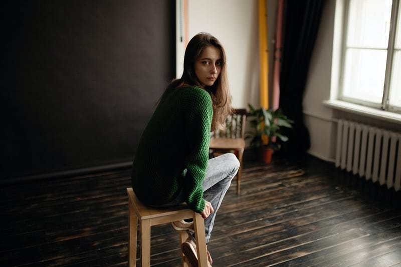 Girl sitting alone in sparse room, gazing at camera