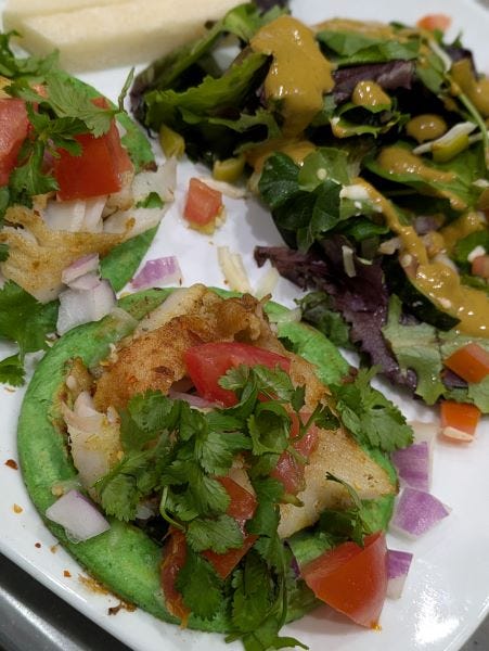 a food picture: green tortilla shells topped with fish, onions, cilantro, tomatoes, and assorted other ingredients, plus a side salad