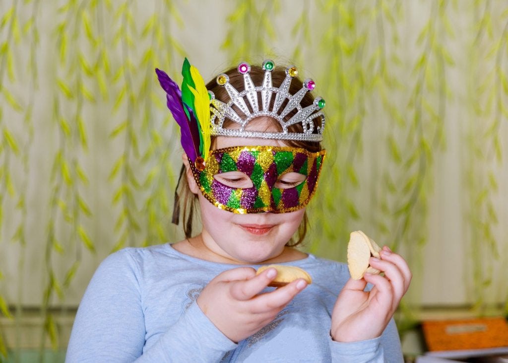 Child wearing a colorful Purim mask and eating hamantaschen