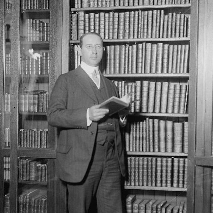 Man standing in front of wall of bookshelves holding open book