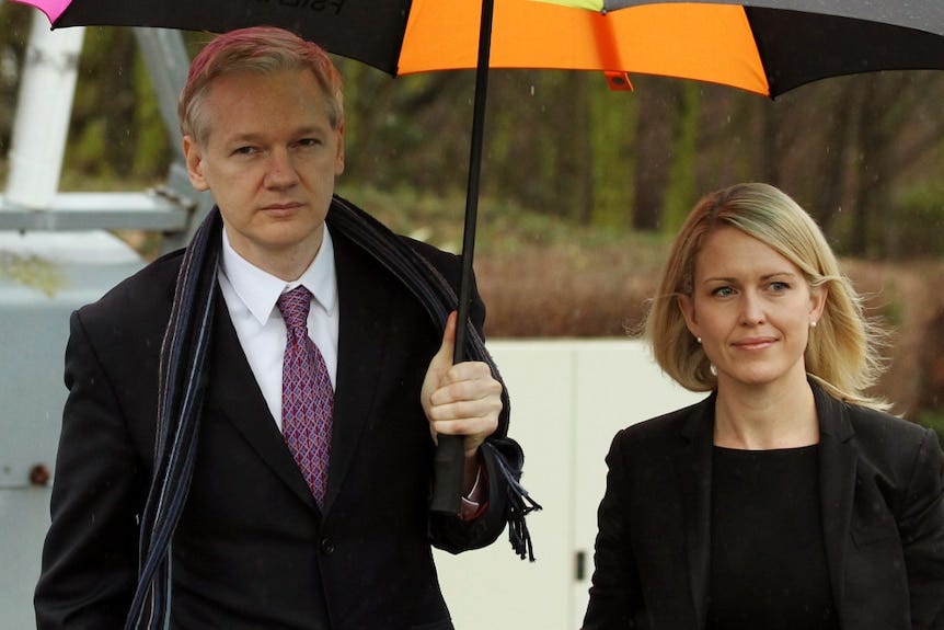 Julian Assange porte un costume tenant un parapluie debout à côté de Jennifer Robinson