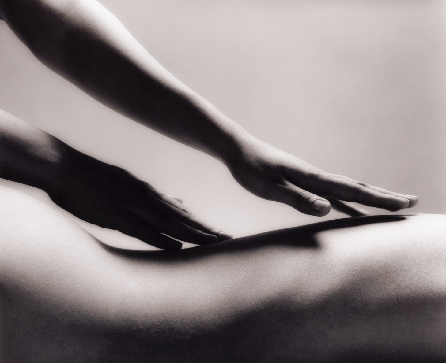 A black and white image of a woman's naked back being massaged by two hands.