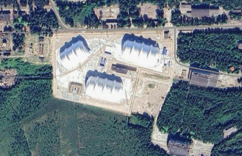 Aerial view of a facility with several large, white, peaked structures surrounded by trees.