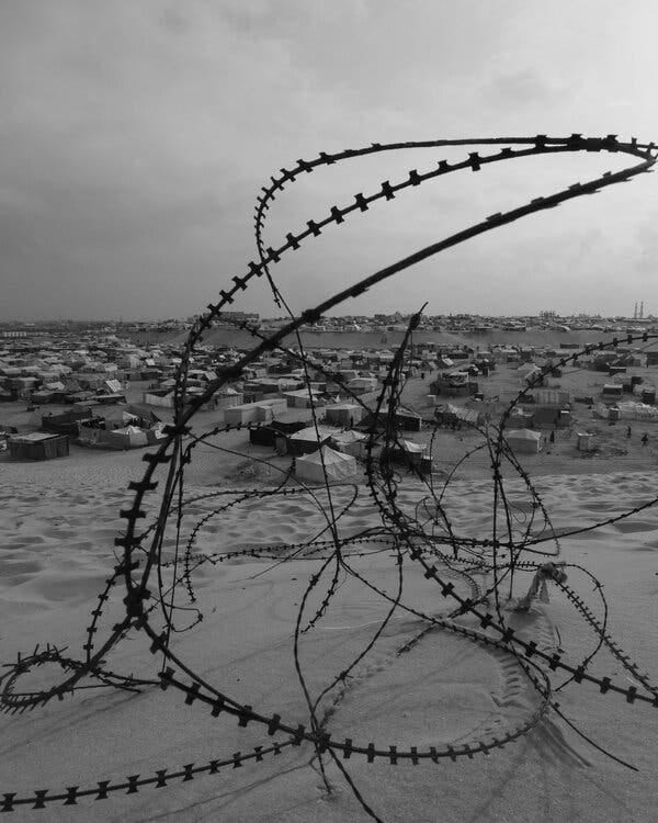 A tangle of barbed wire rests in the sand in front of a camp for displaced Palestinians in Rafah.