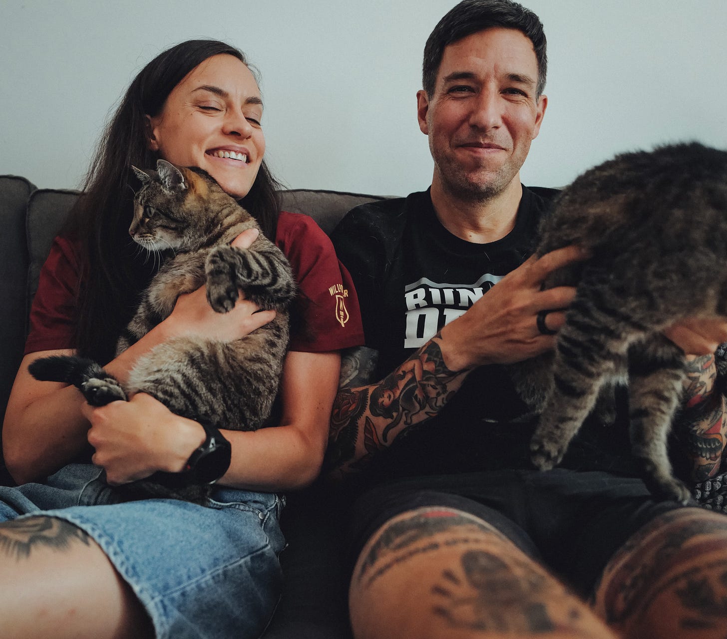 Chris and Lisa with their two cats on a couch with one cat jumping out of the picture