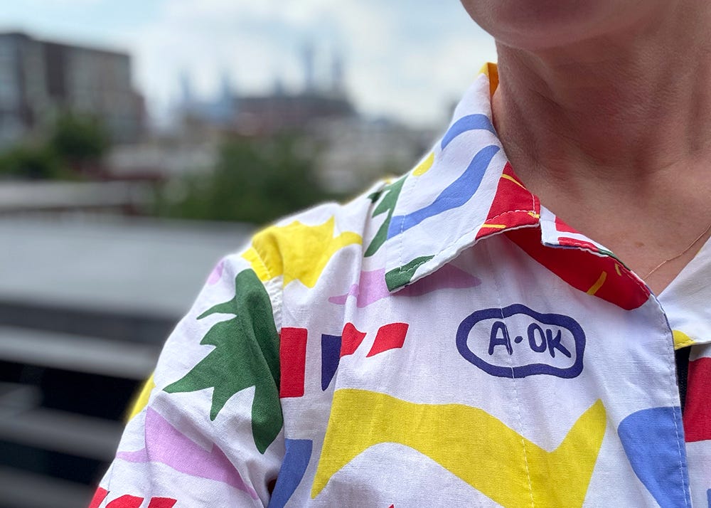 Yellow, red, green, and blue abstract shapes on a white shirt worn by a white woman - with a blurred city view in the background. Yellow, red, green, and blue abstract shapes on a white shirt worn by a white woman - with a blurred city view in the background.