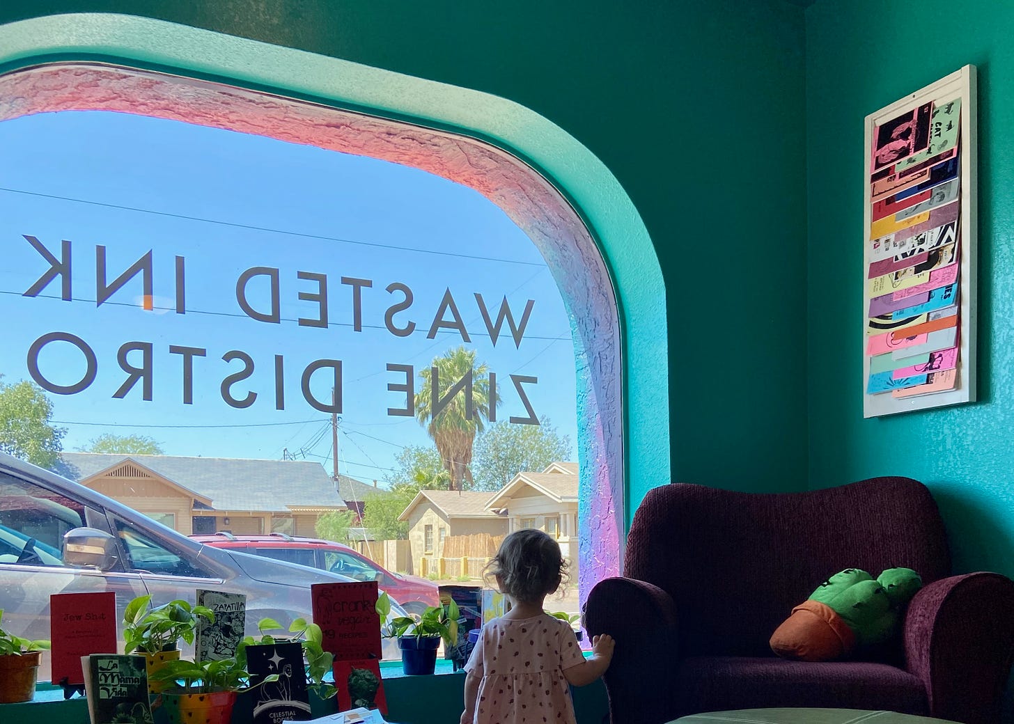 The reading nook at Wasted Ink featuring a comfy purple chair, teal walls, and my young daughter looking out the window