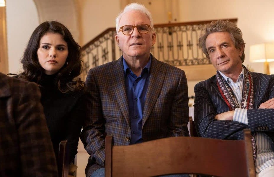 Photo from the show Only Murders in the Building that shows actors Selena Gomez, Steve Martin, and Martin Short sitting in a row with serious looks on their faces.