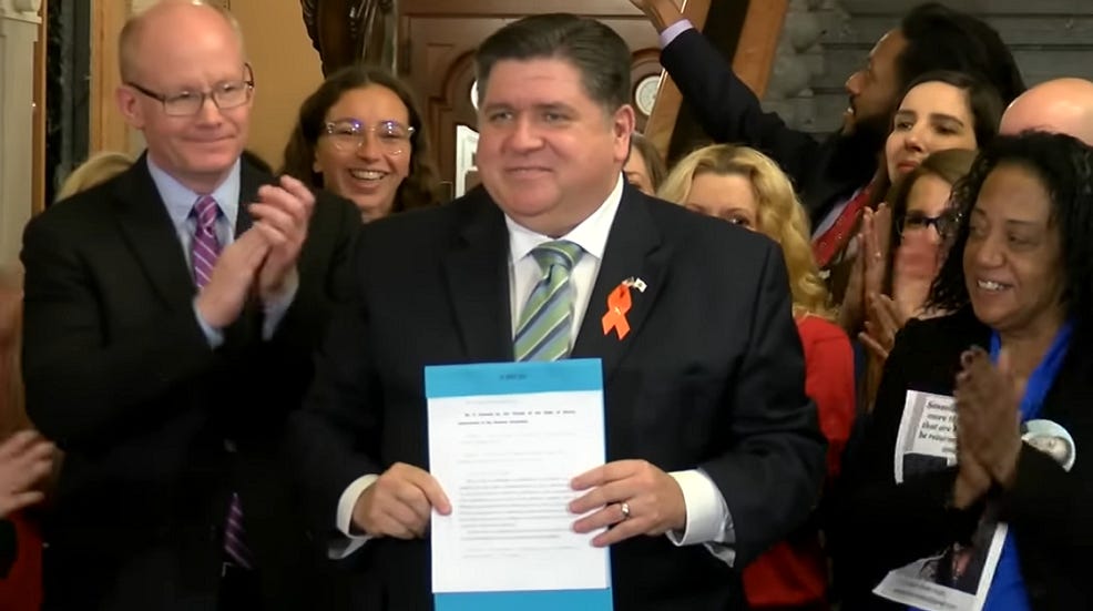 Illinois governor JB Pritzker poses with a copy of his new gun control law.