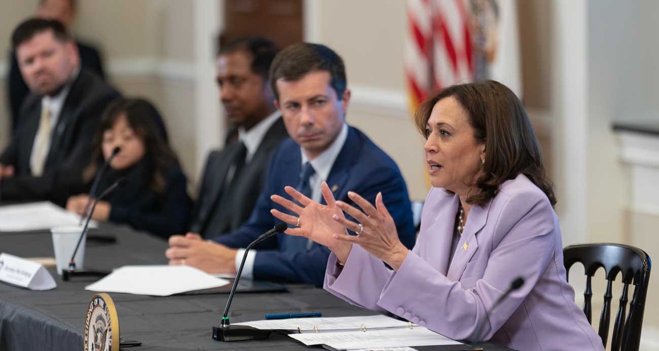 Kamala Harris speaking while seated at a table next to the Transportation Secretary.