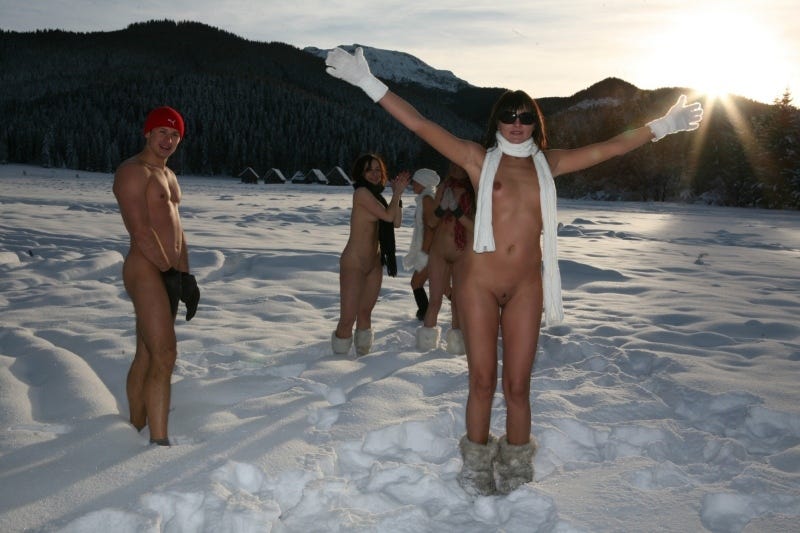 A set of friends naked on a patch of snow wearing only snow boots, hats and scarves.