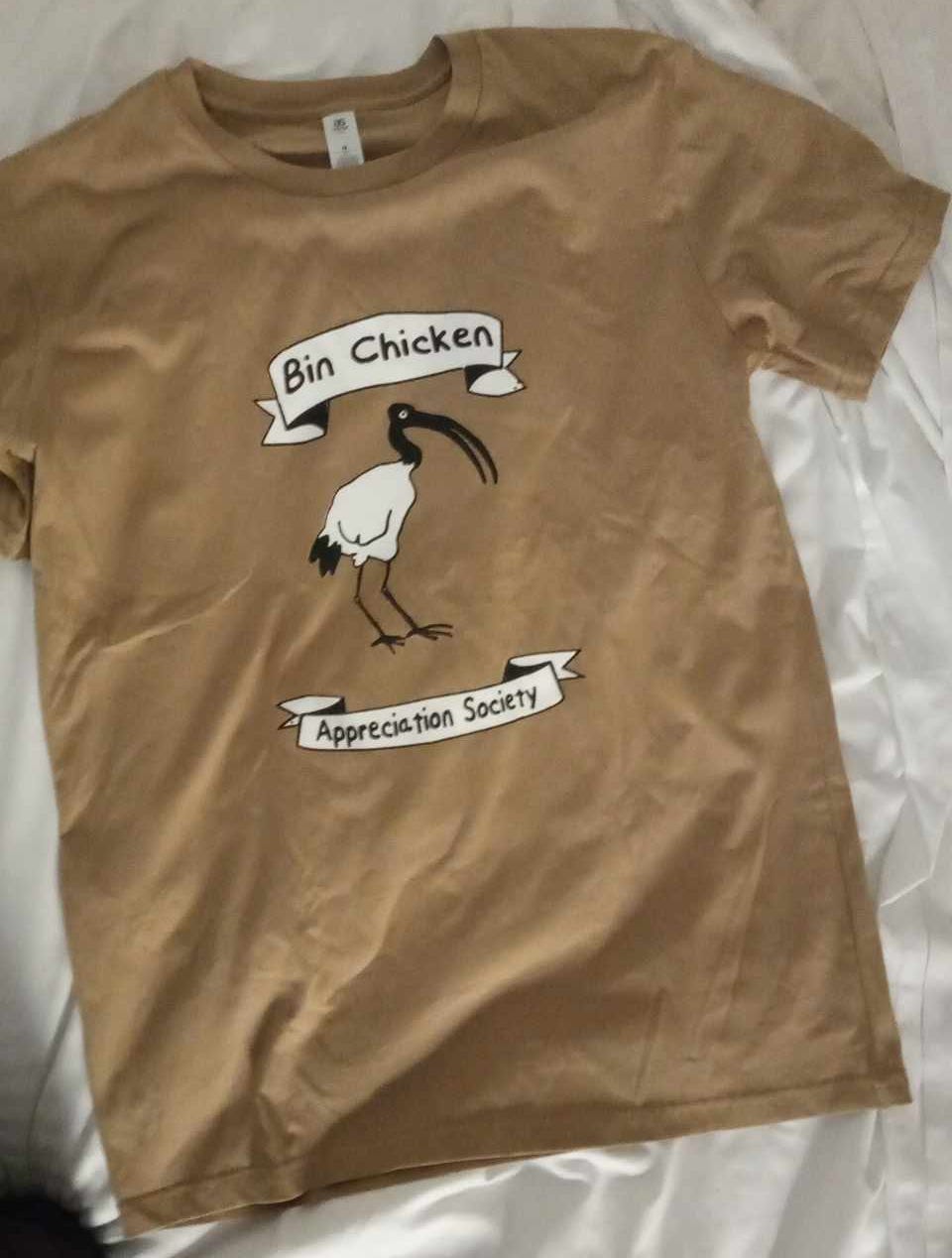 a t-shirt spread on a bed. The shirt has an image of an Ibis bird, and has banners reading "Bin Chicken Appreciation Society"
