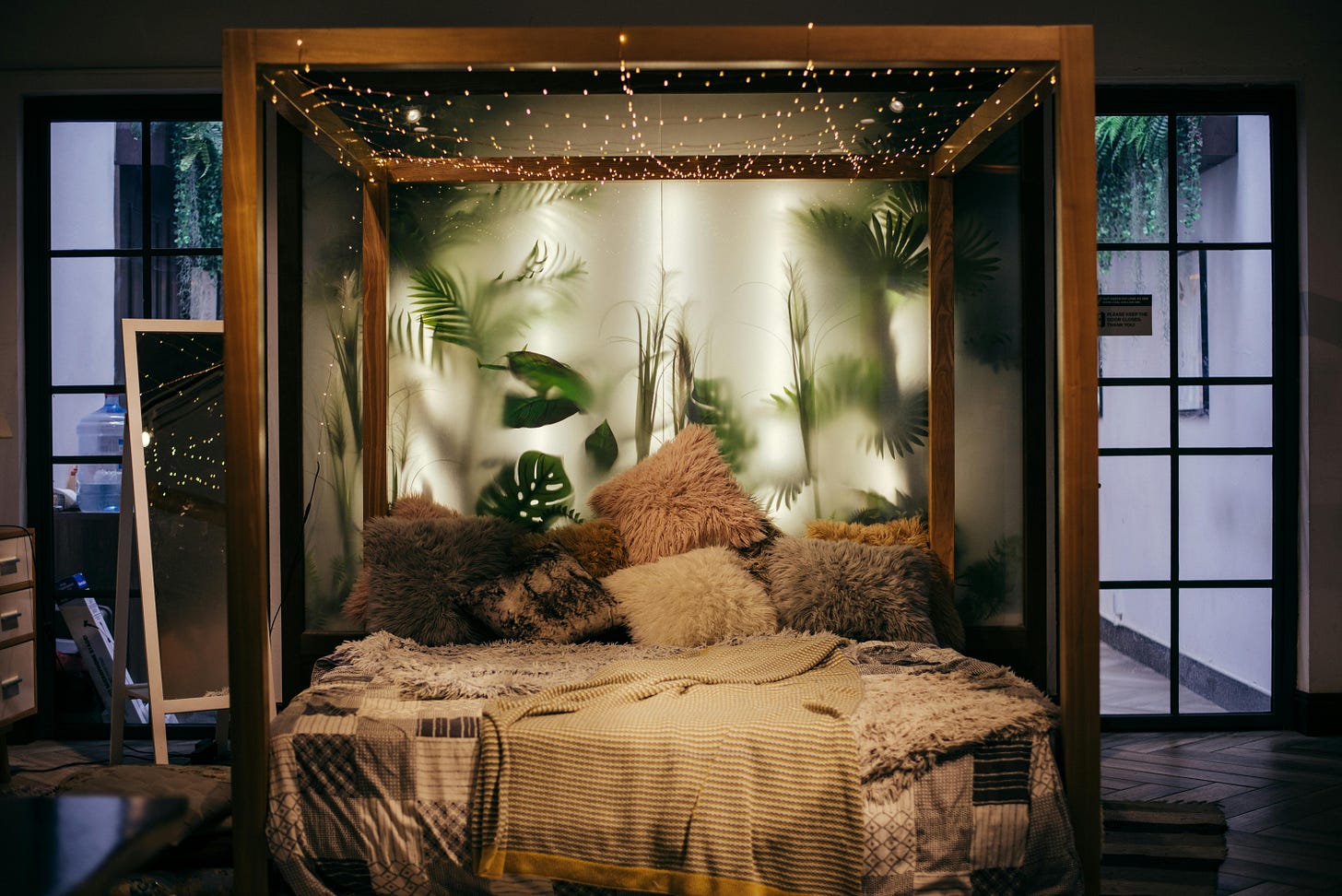 A brown wooden canopy bed, draped with fairy lights. Cozy blankets and pillows are strewn across it.