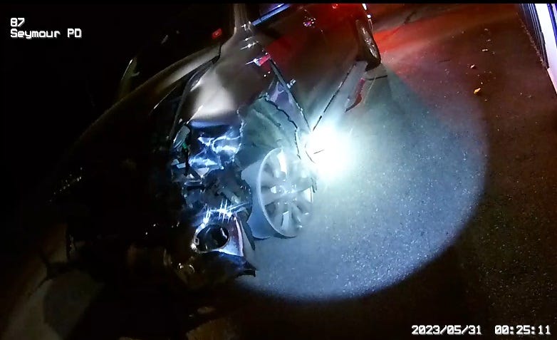a police photo of a wrecked van lit by a cop's flashlight, its front wheel rim down to the bare metal 
