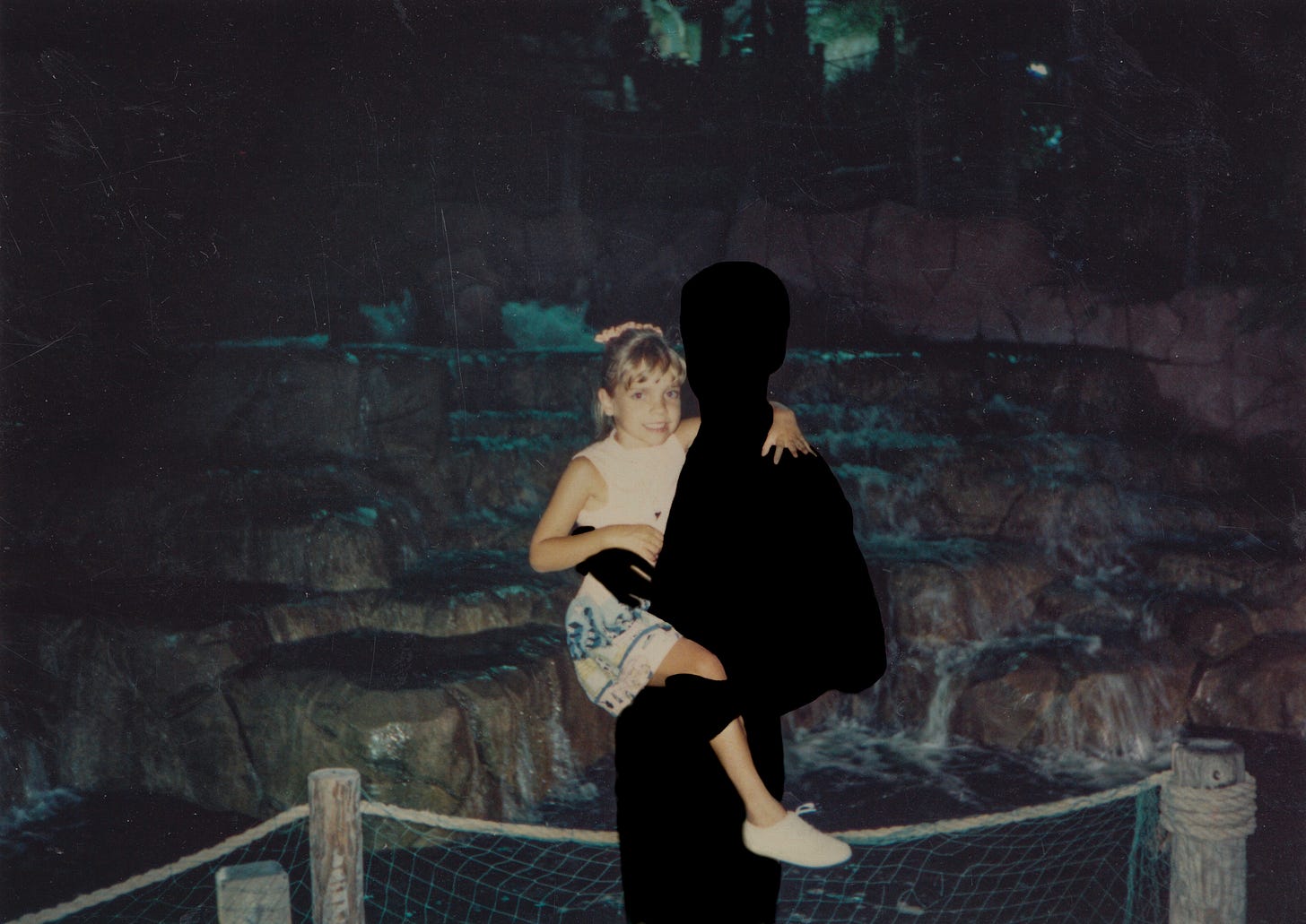 My brother and I at a mini golf waterfall at night. He is silhouetted and holding me. I am about 8 years old.