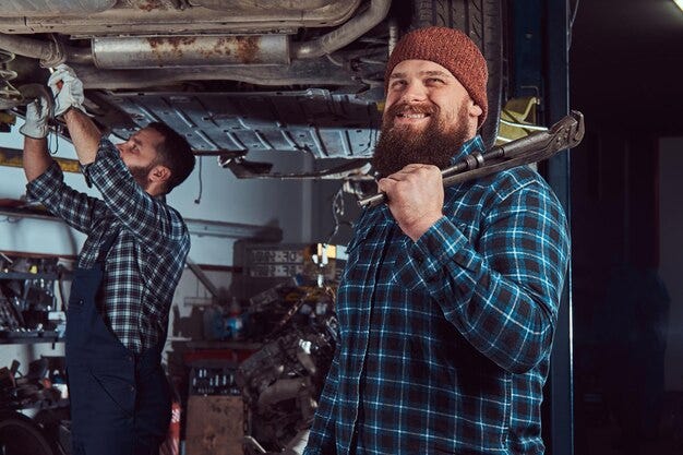 Free photo two bearded brutal mechanics repair a car on a lift in the garage. repairing car suspension in a service station.