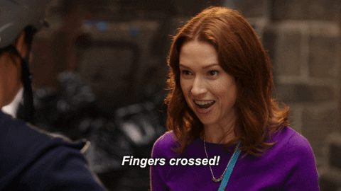 A GIF of Kimmy from Unbreakable Kimmy Schmidt saying, "Fingers crossed!" and excitedly crossing her fingers on both hands.