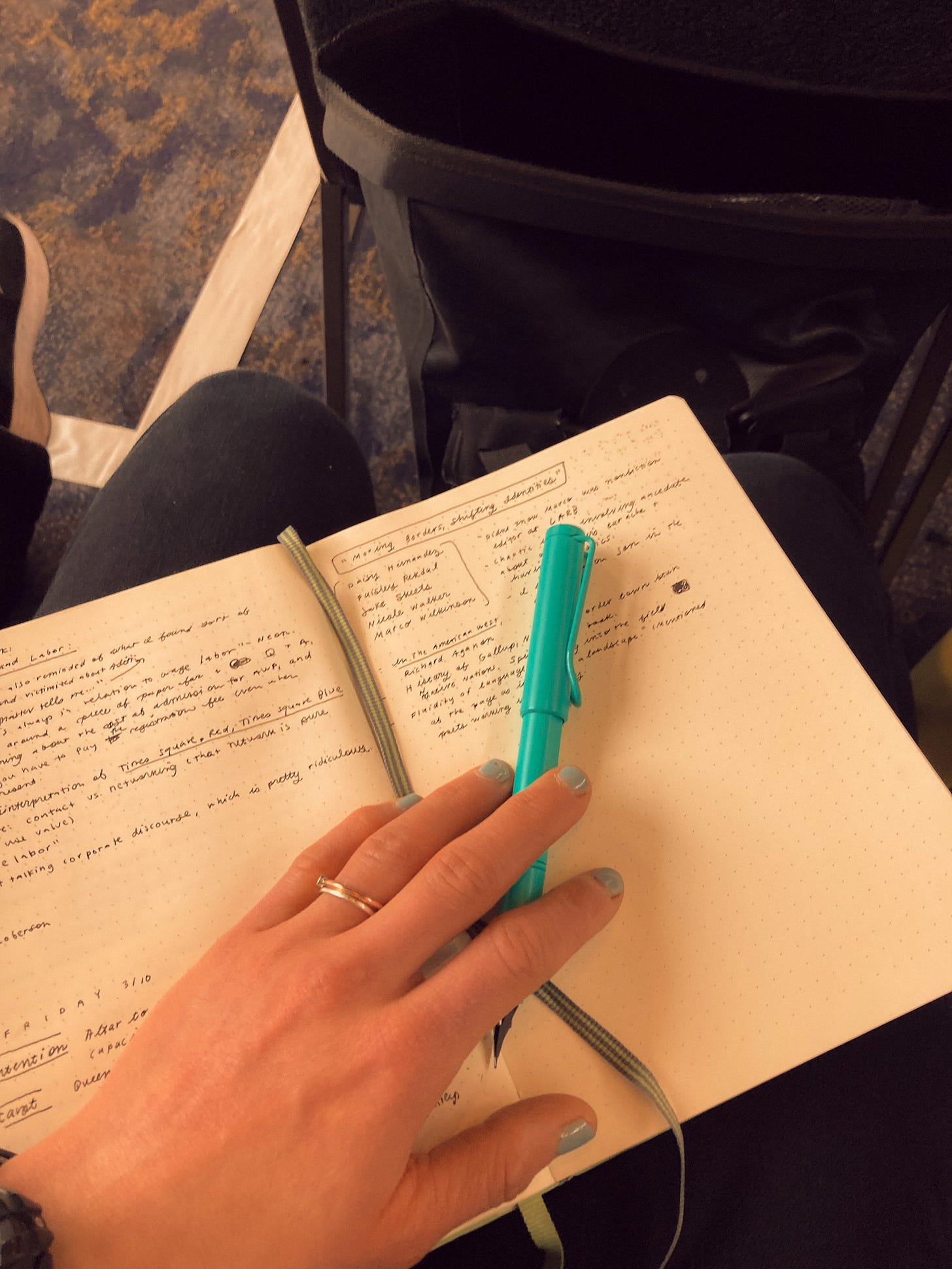 Siloh's hand on a notebook with a green pen. The pages are partially filled with handwriting.