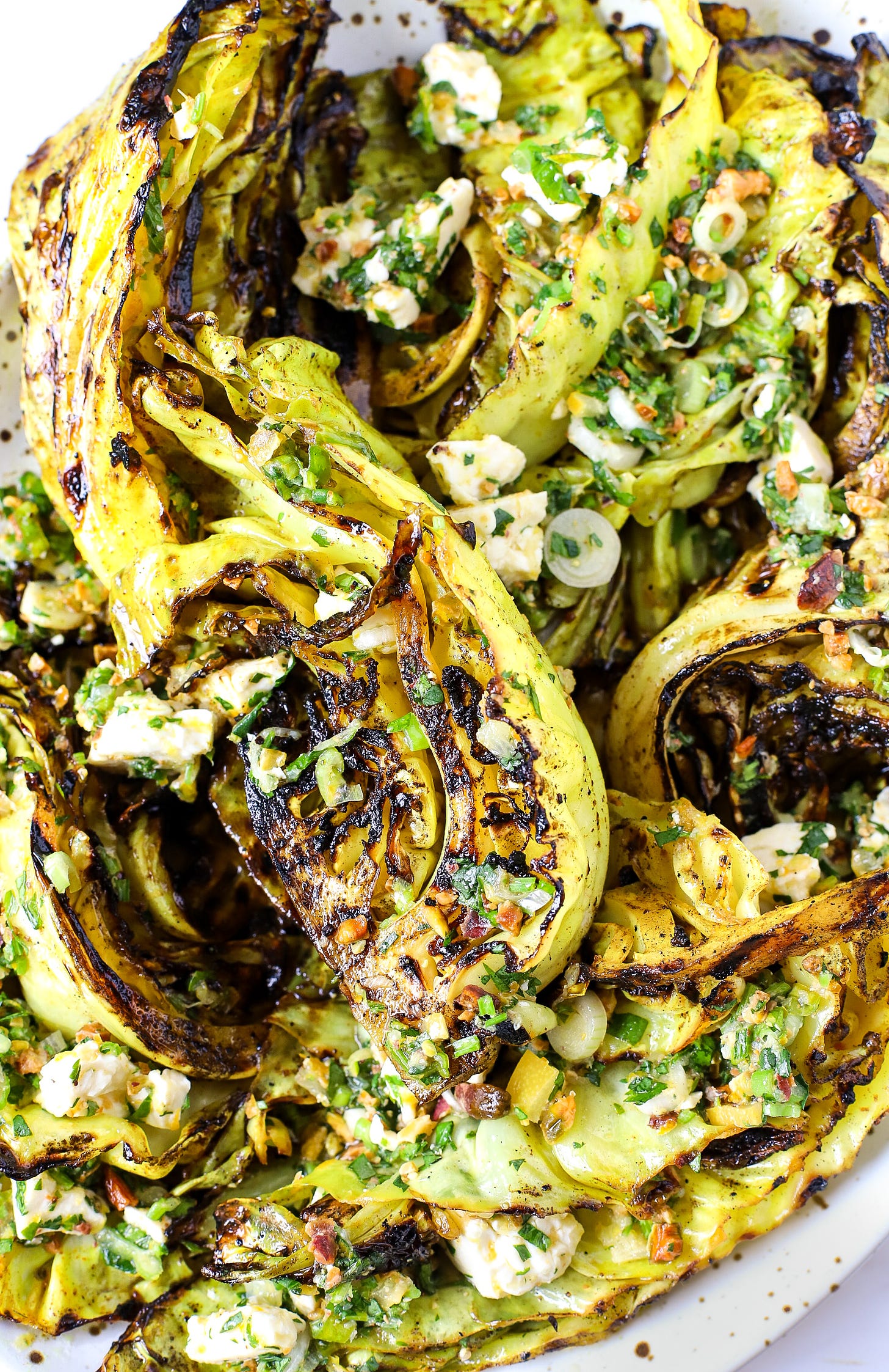 Wedges of char-grilled cabbage with dressing, feta, and nuts