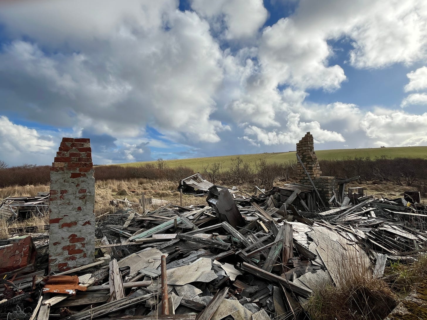 Photo of the derelict house, you can see the piano standing upright in between 2 chimney stacks in a pile of wooden 'rubble'