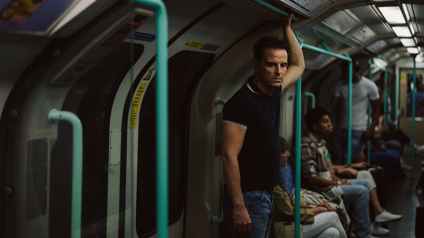 Foto do ator Andrew Scott como Adam, com expressão apática, em um escuro metrô.