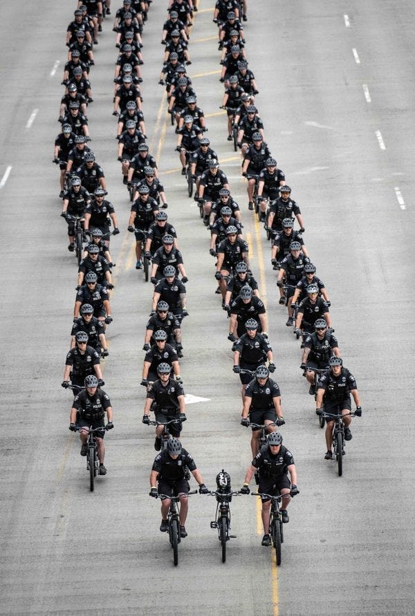 Defile de policier dont deux a l'avant tenant un troisieme velo sans cycliste