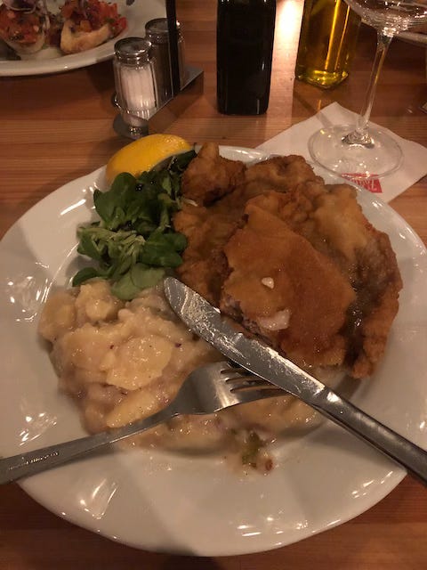 Picture of a white plate with schnitzel, potato salat, watercress and cutlery