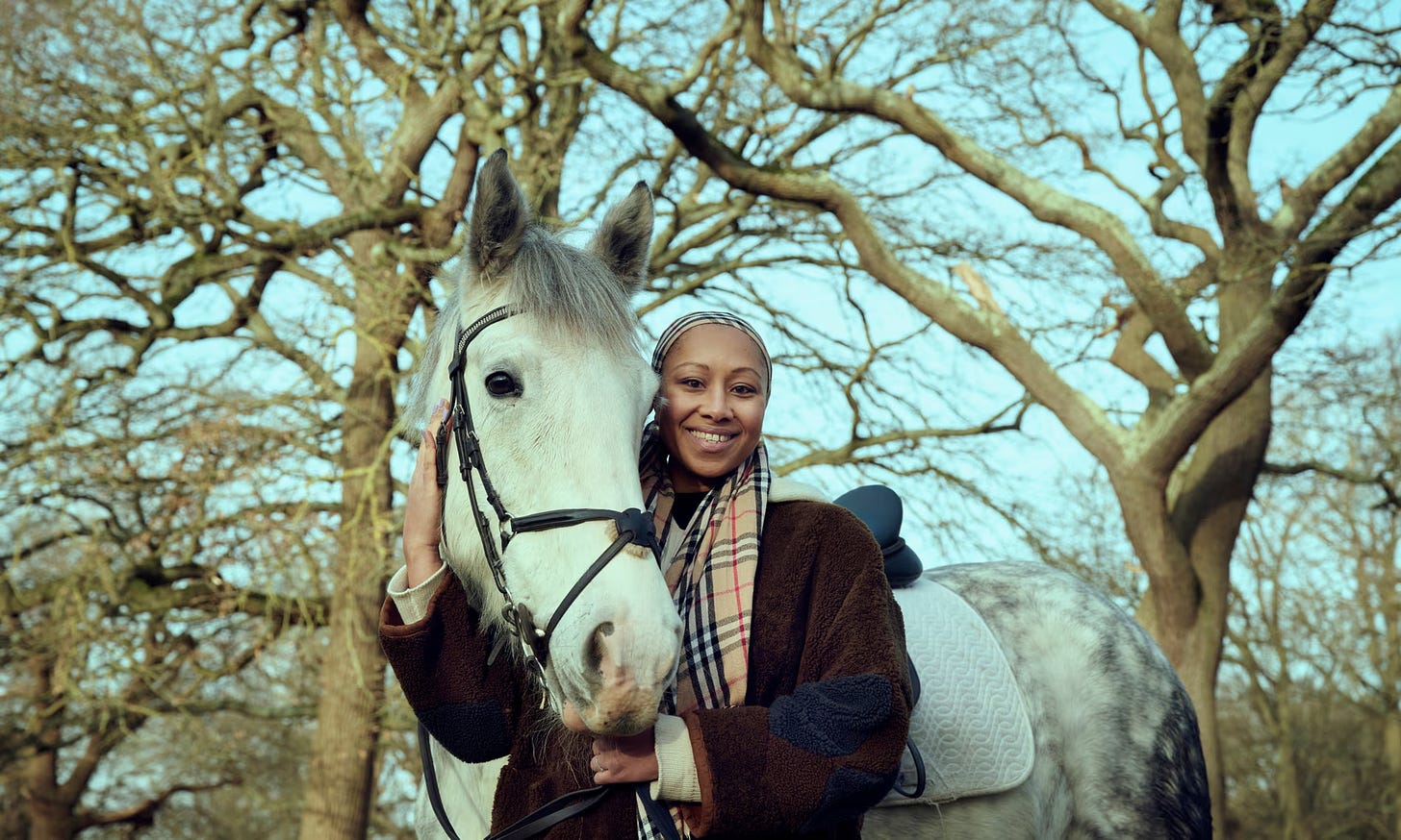 Standing with a grey dappled horse, the horse's head close to Yassmin's her hand wrapped around his head (horse's name is flint)