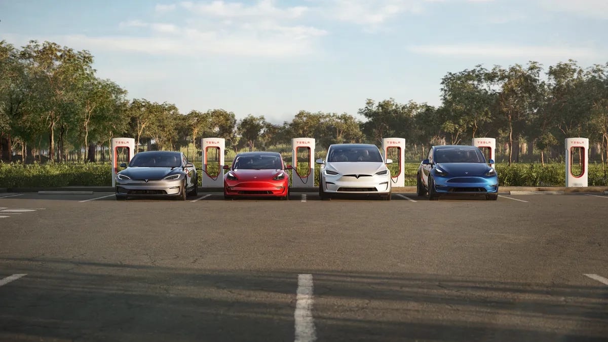 The lineup of Tesla vehicles parked at a Supercharger with tress in the background in a media photo.