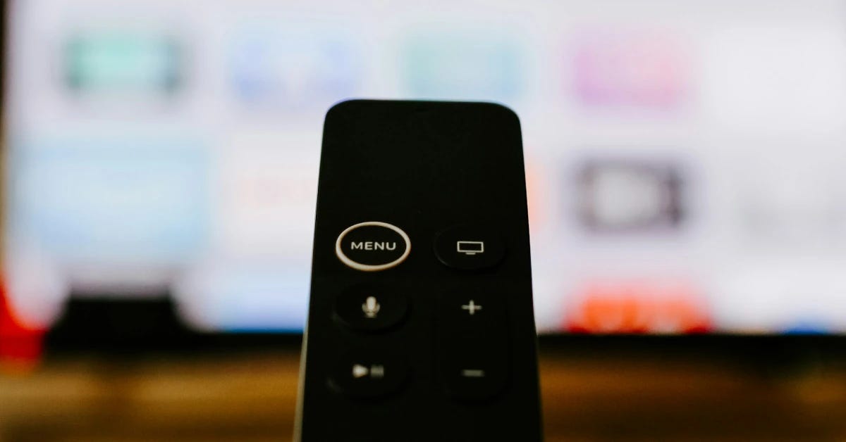 An Apple TV remote in front of a blurry television set.
