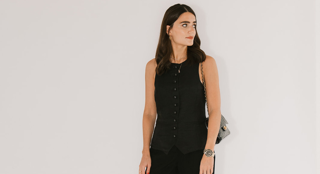 A picture of Bee Newham - a woman with brown hair wearing a black outfit, standing in front of a black background