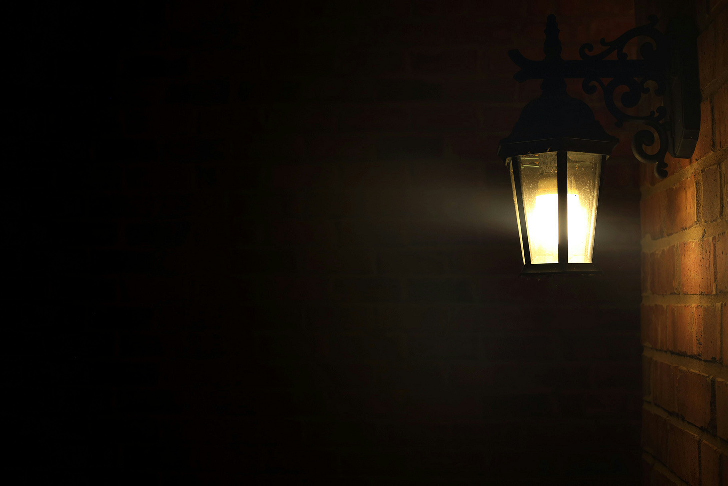 a single old fashioned looking porch light glowing, illuminating part of the brick behind it