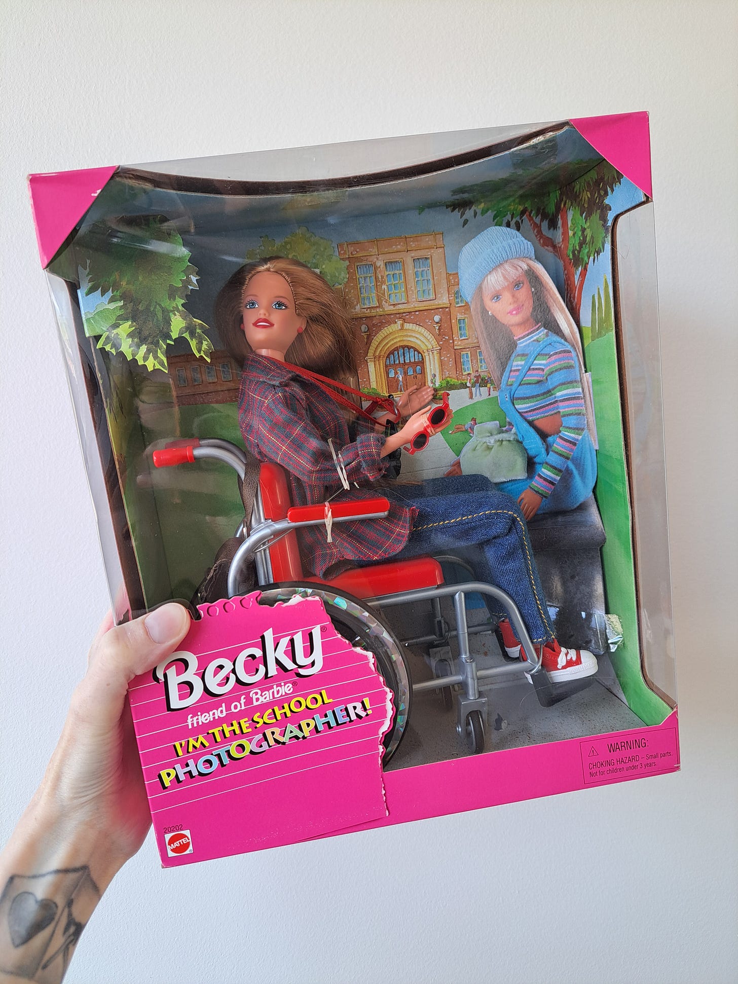 My hand holding Becky, a Barbie doll in a wheelchair in the original packaging.