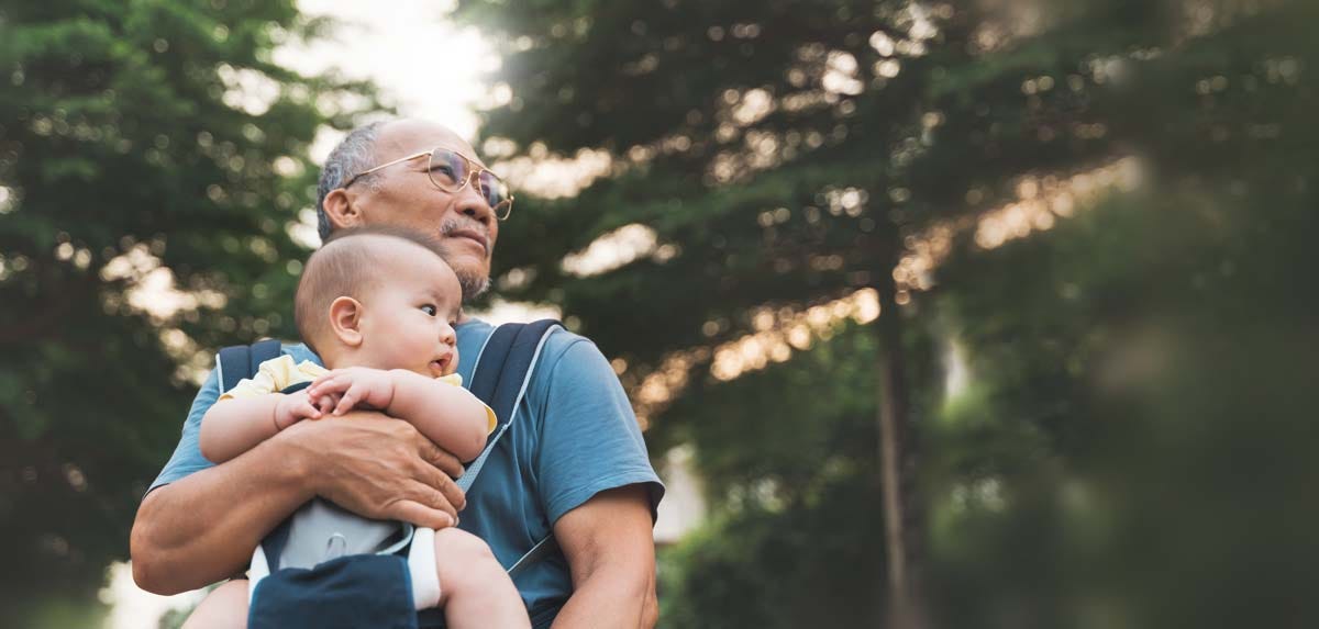 Asian Grandfather carrying his Little Grandson in baby carrier walking at park outdoor.