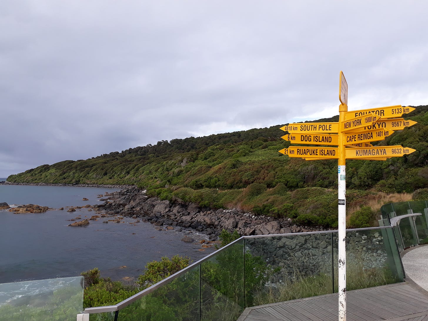 The image shows a sign post which point in different directions beside a coastline and sea. You can see an arrow pointing to the South Pole which is 4810km, New York 1508 km, Equator which is 5133km.