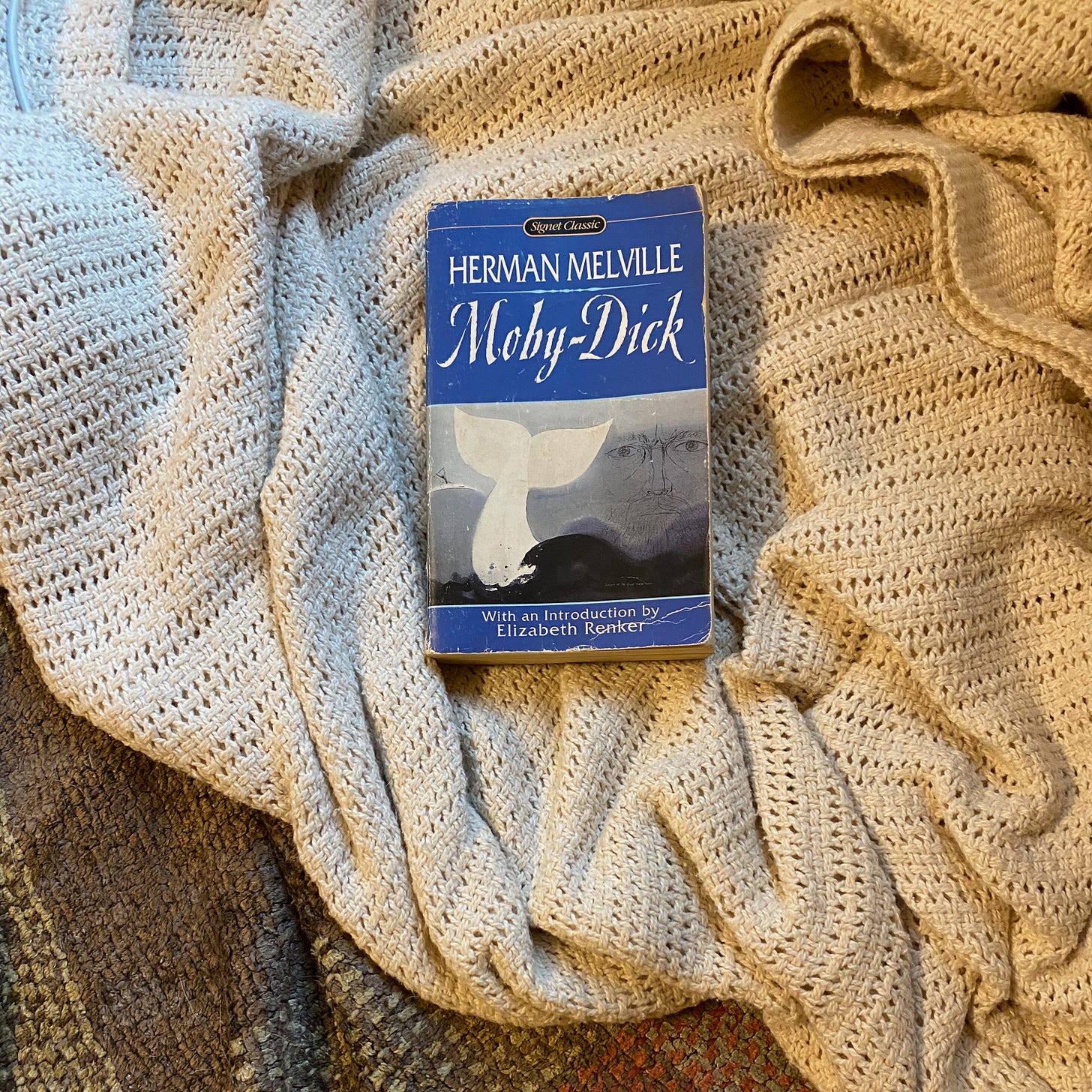 A small blue paperback copy of Moby-Dick lying on top of a white blanket.