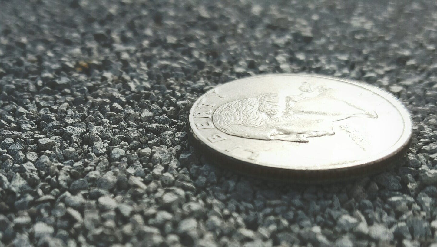 A US quarter lying heads up on a packed gravel surface