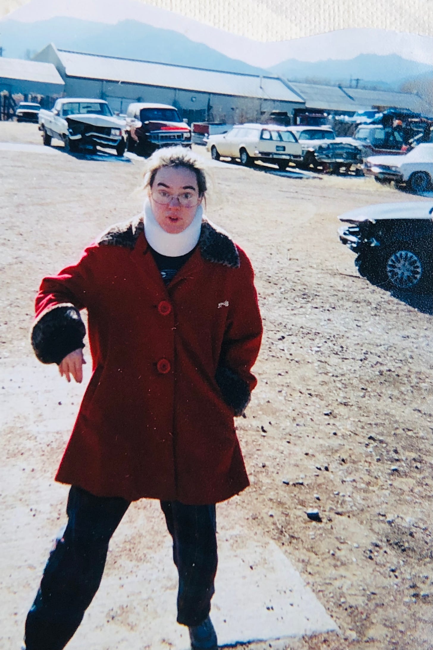 The slack-jawed, huge-eyed author in a neck brace, glasses, sweats and messy hair, as well as a swanky red coat with faux leopard trim. Looking like a startled cat amidst a slew of totaled vehicles with the Colorado mountains in the background. 