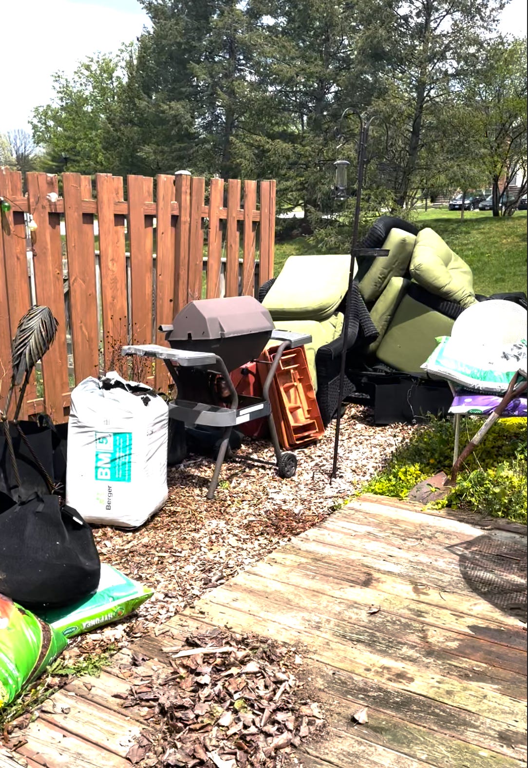 4. A photo of the back garden including a large pile of hastily stacked outdoor furniture and cushions, outdoor equipment and a barbecue.