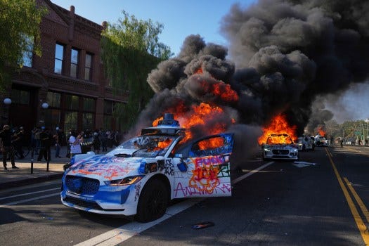 Multiple Waymo taxis burn Sunday near the Metropolitan Detention Center of downtown Los Angeles. (AP Photo/Eric Thayer)