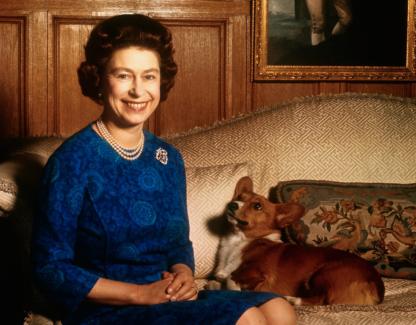 Queen Elizabeth II sitting with a corgi and smiling