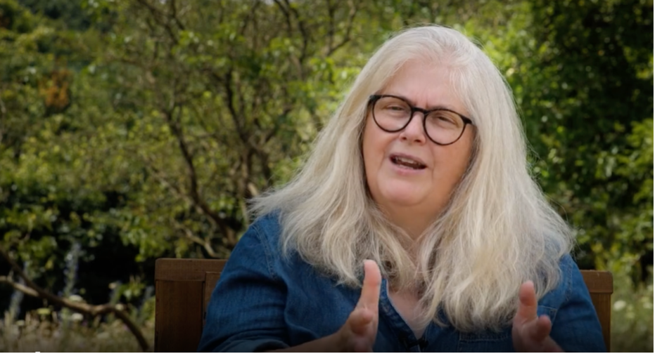 Sally Wainwright, a woman with long grey hair sits in front of some green trees
