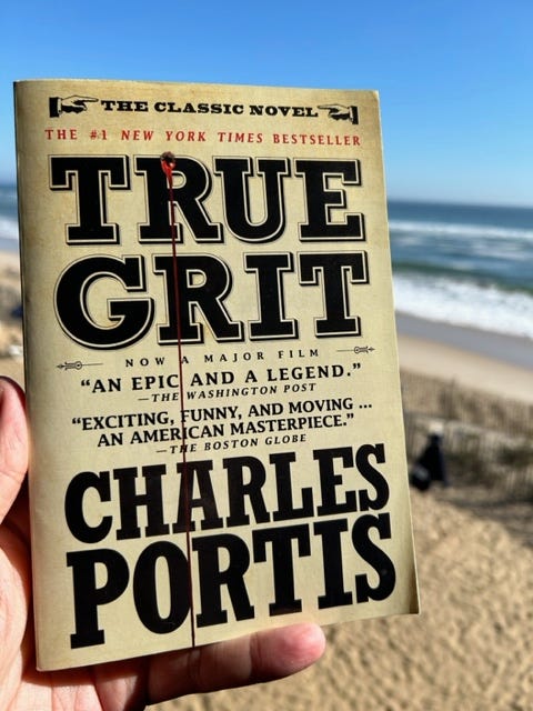 True Grit by Charles Portis is held up with a beach in the background