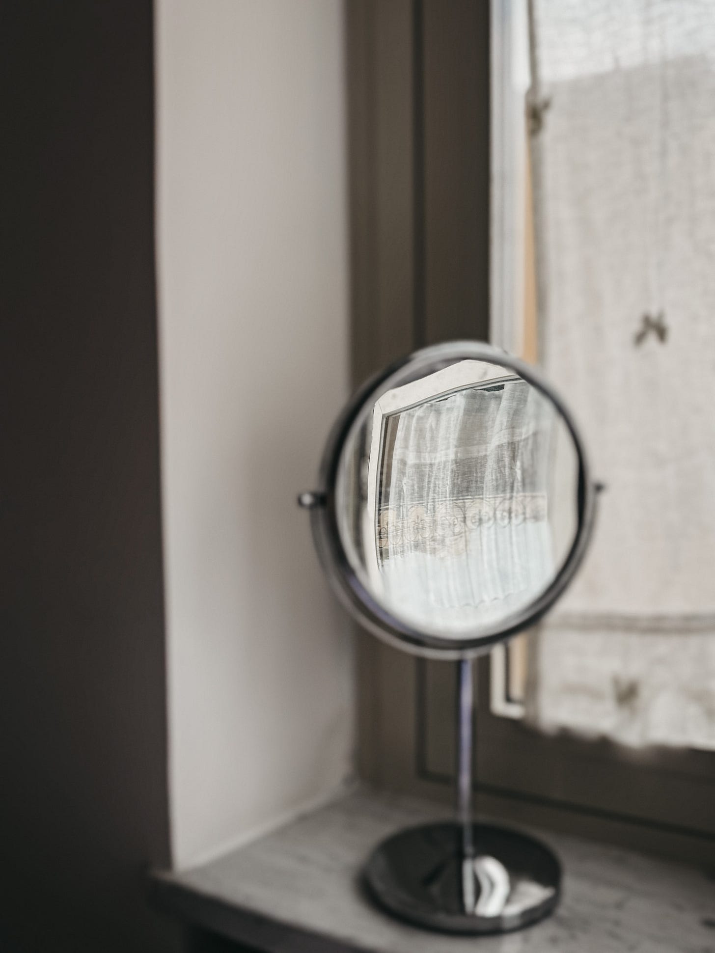 A small round mirror catching light on a windowsill, reflecting the soft tones of a quiet Roman interior.