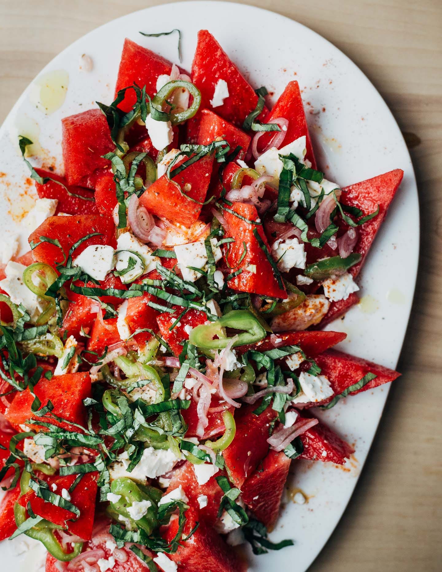 A watermelon salad with chilies and herbs arranged on a platter. 