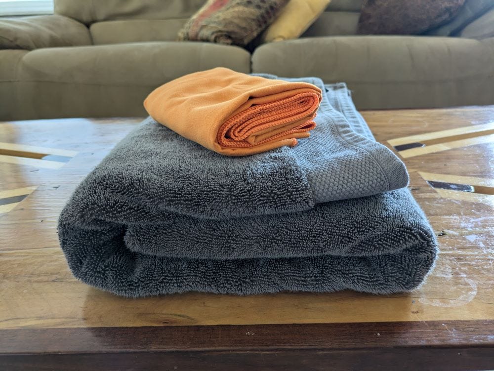 two towels on a coffee table, one large grey terry cloth, and one small orange chamois-like fabric, both folded neatly