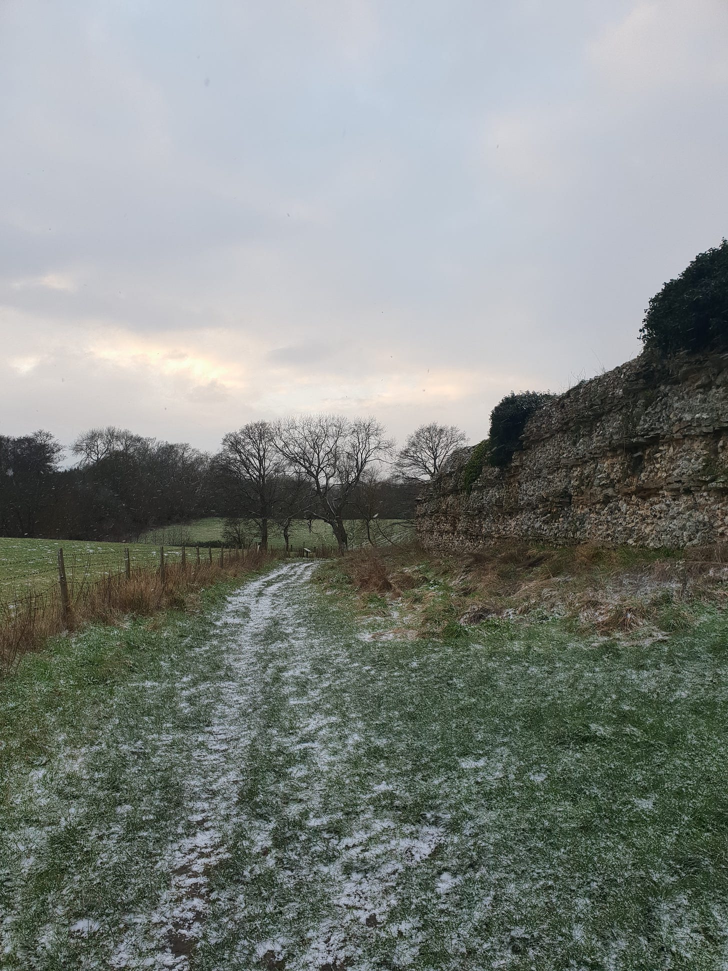 Snow-covered grass track running alongside a tall, stone Roman wall