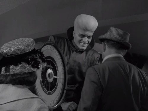 Still image from the Twilight Zone episode, "To Serve Man". Woman and man in the FG facing an alien with a weird forehead standing in front of a space ship engine.