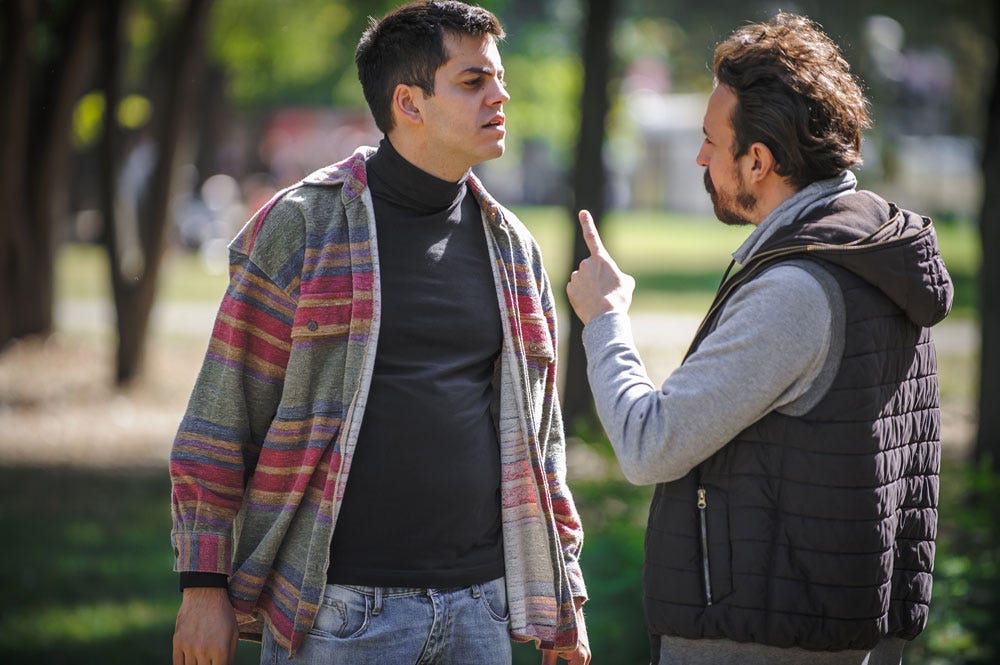 Two people outside in a park arguing, one blaming the other.